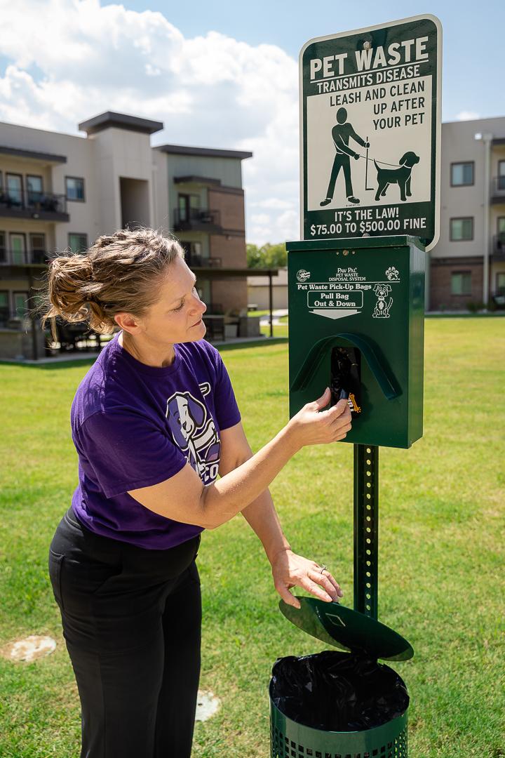Simply Scoop team member performing commercial pet waste removal on apartment community grounds.